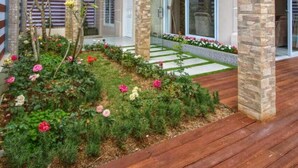 A modern two-story house with a balcony, stone pillars, and a garden with flowers. - Villa Kota Bunga Puncak 4 Bedroom (Cipanas)