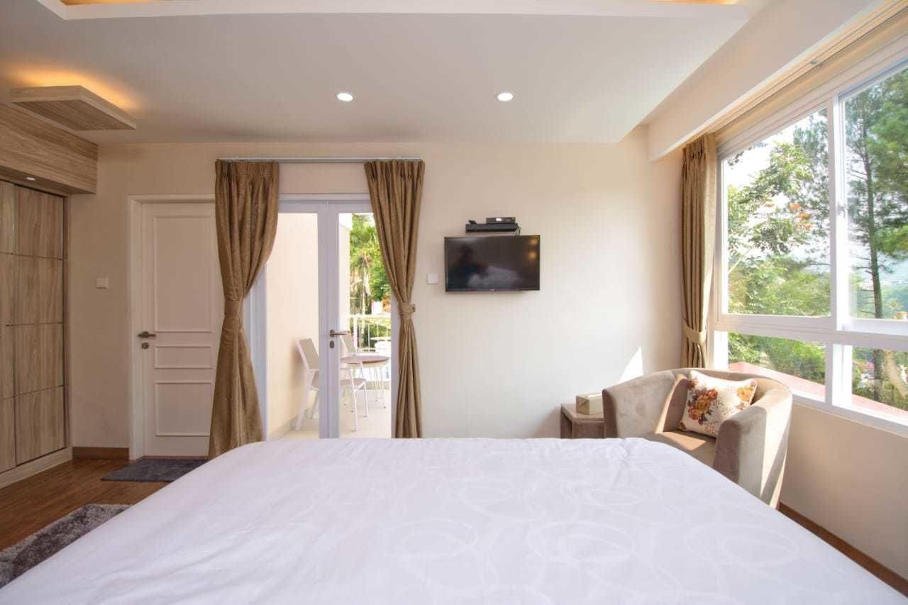 Un dormitorio con una cama grande, un televisor en la pared y un ventanal con cortinas.