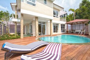 A two-story house with a swimming pool, lounge chairs, and a covered patio area. - Villa Kota Bunga Puncak 4 Bedroom (Cipanas)