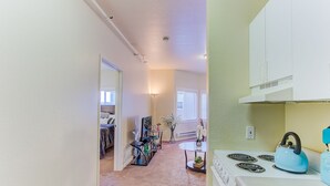 A compact kitchen with white cabinets, a stove, and a kettle. A dining area with a table and chairs is visible in the background. - Cosy Berkeley Apartments Across UC Berkeley #121 (Berkeley)