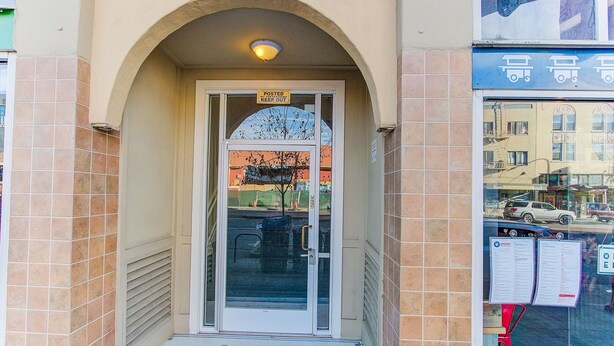 A building entrance with a posted sign, a tiled entrance, and a visible street view through the window. - Cosy Berkeley Apartments Across UC Berkeley #121 (Berkeley)