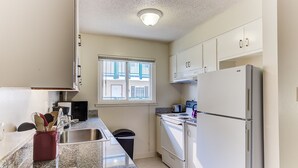 A compact kitchen with a stainless steel sink, a gas stove, a white refrigerator, and a window with blinds.