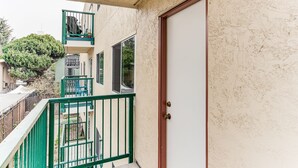 Un bâtiment doté d’une rambarde métallique verte, d’une porte blanche et d’un balcon avec une chaise.