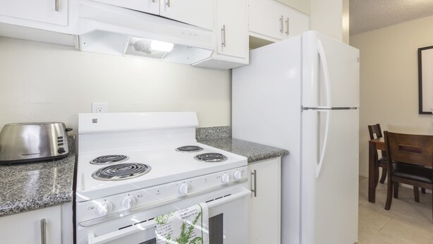 Eine Küche mit weißen Schränken, einem weißen Herd, einem weißen Kühlschrank, einem Toaster und einer Arbeitsplatte aus Granit.