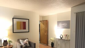 A living room with a grey armchair, a framed picture, a wooden door, a console table with a potted plant, and a 'Home' sign on the wall. - Cosy Berkeley Apartment Close to UC Berkeley #E (Berkeley)