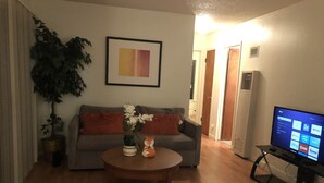 A living room with a gray sofa, a round wooden coffee table, a potted plant, and a flat-screen TV on a stand. - Cosy Berkeley Apartment Close to UC Berkeley #E (Berkeley)
