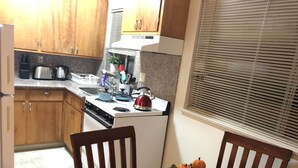 A compact kitchen with wooden cabinets, a stove, and a sink. There is a dining table with chairs and a decorative centerpiece. - Cosy Berkeley Apartment Close to UC Berkeley #E (Berkeley)