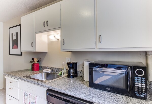 A compact kitchen with white cabinets, a built-in microwave, a coffee maker, and a dishwasher.