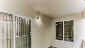 Quarto com porta de vidro deslizante, janela com persianas e luminária na parede.