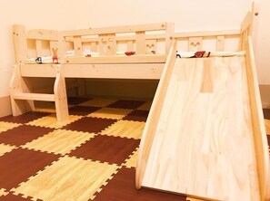 Ein Holzbett mit Etagen und einer Leiter, ein karierter Boden und ein kleines Spielzeug auf dem Bett.