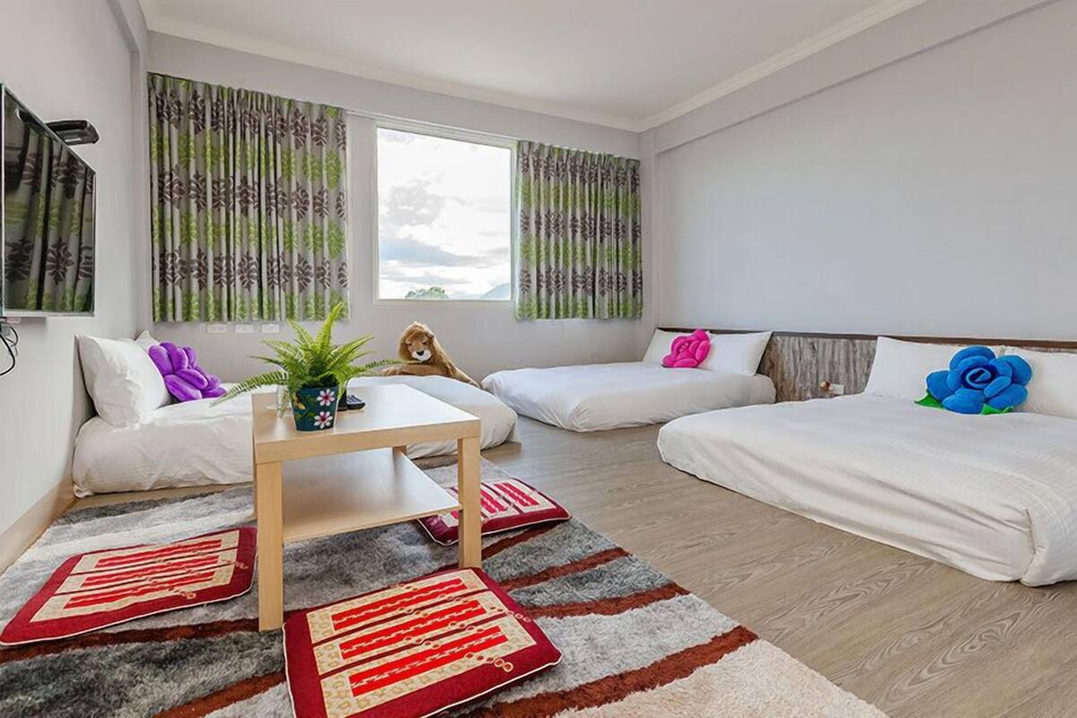 A modern hotel room with two single beds, a sofa, a small table, and a large window with curtains.