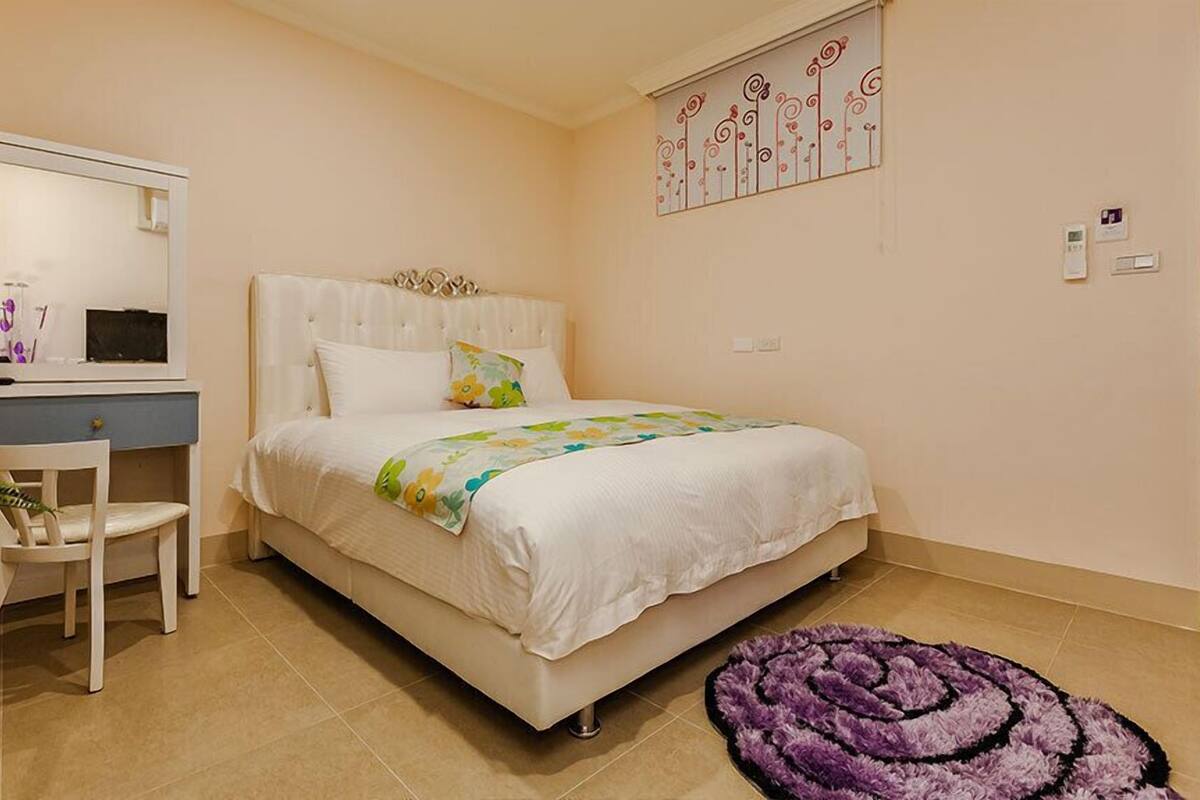 A bedroom with a bed, a desk, a chair, and a purple rug.