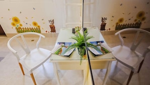 A dining area with a glass table, white chairs, and a fern centerpiece.