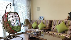 A living room with a striped sofa, green cushions, a hanging chair with a green seat, and a glass coffee table.