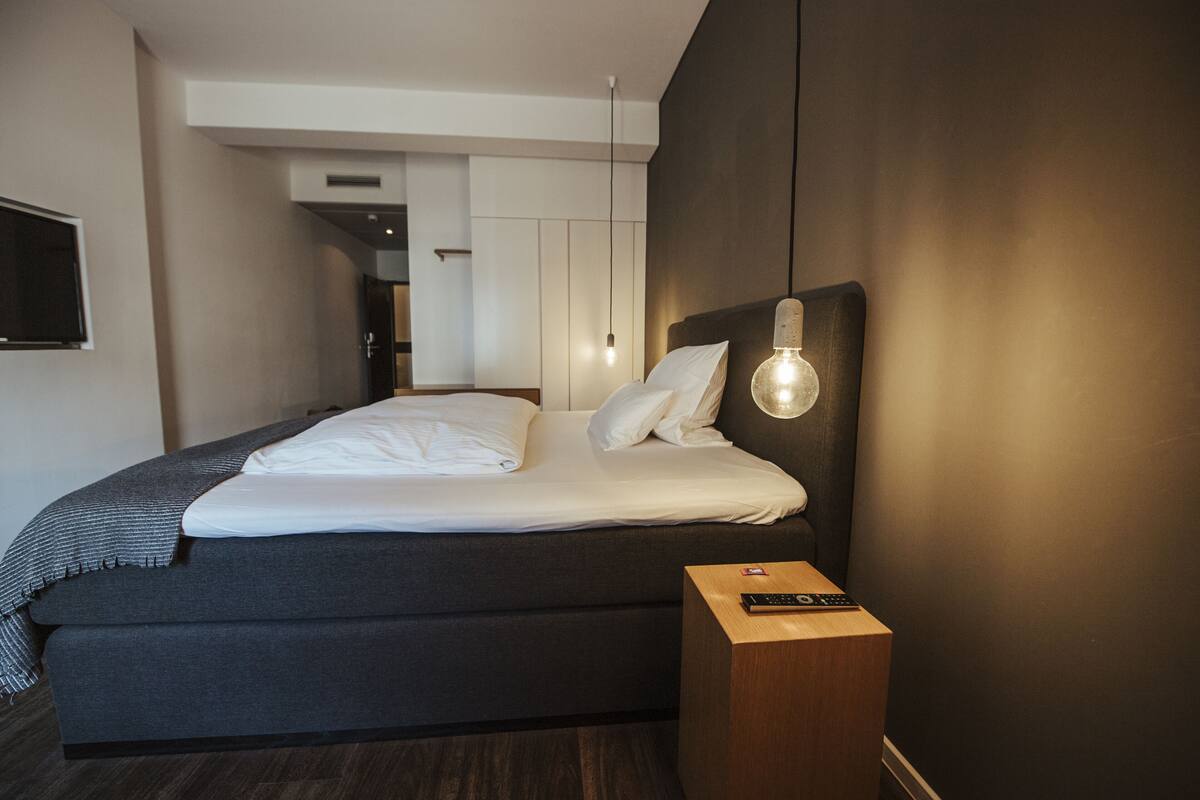 Ein modernes Hotelzimmer mit einem großen Bett, einem Nachttisch mit Fernbedienung und einer Wandleuchte.
