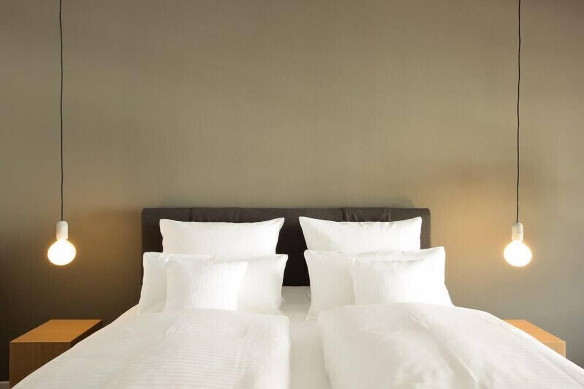 Ein Doppelbett mit weißer Bettwäsche, einem dunklen Kopfteil und zwei hängenden Lampen.