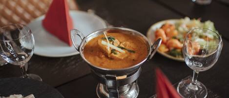 A dining table with a metal bowl of soup, a plate of shrimp, and a red napkin.