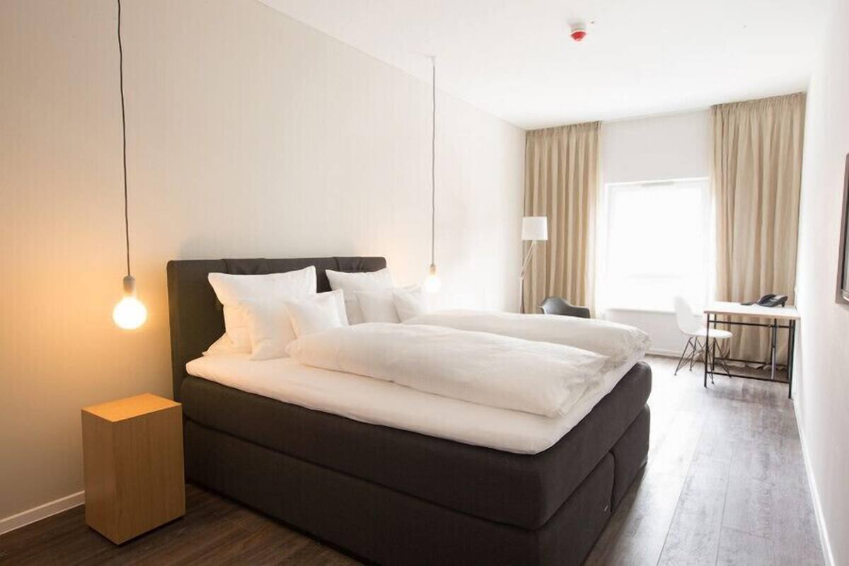 Ein Hotelzimmer mit Bett, Nachttisch, Lampe und Schreibtisch mit Stuhl.