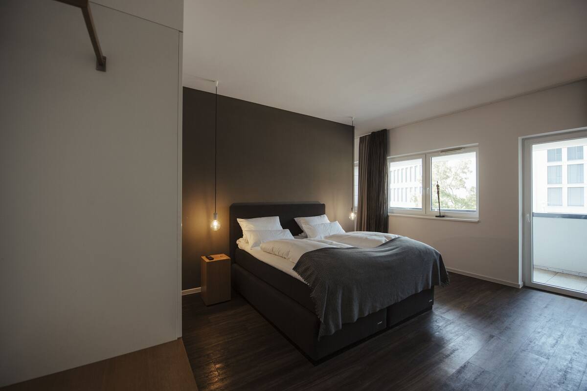 Ein modernes Schlafzimmer mit einem großen Bett, einem Nachttisch und einem Fenster mit Vorhängen.
