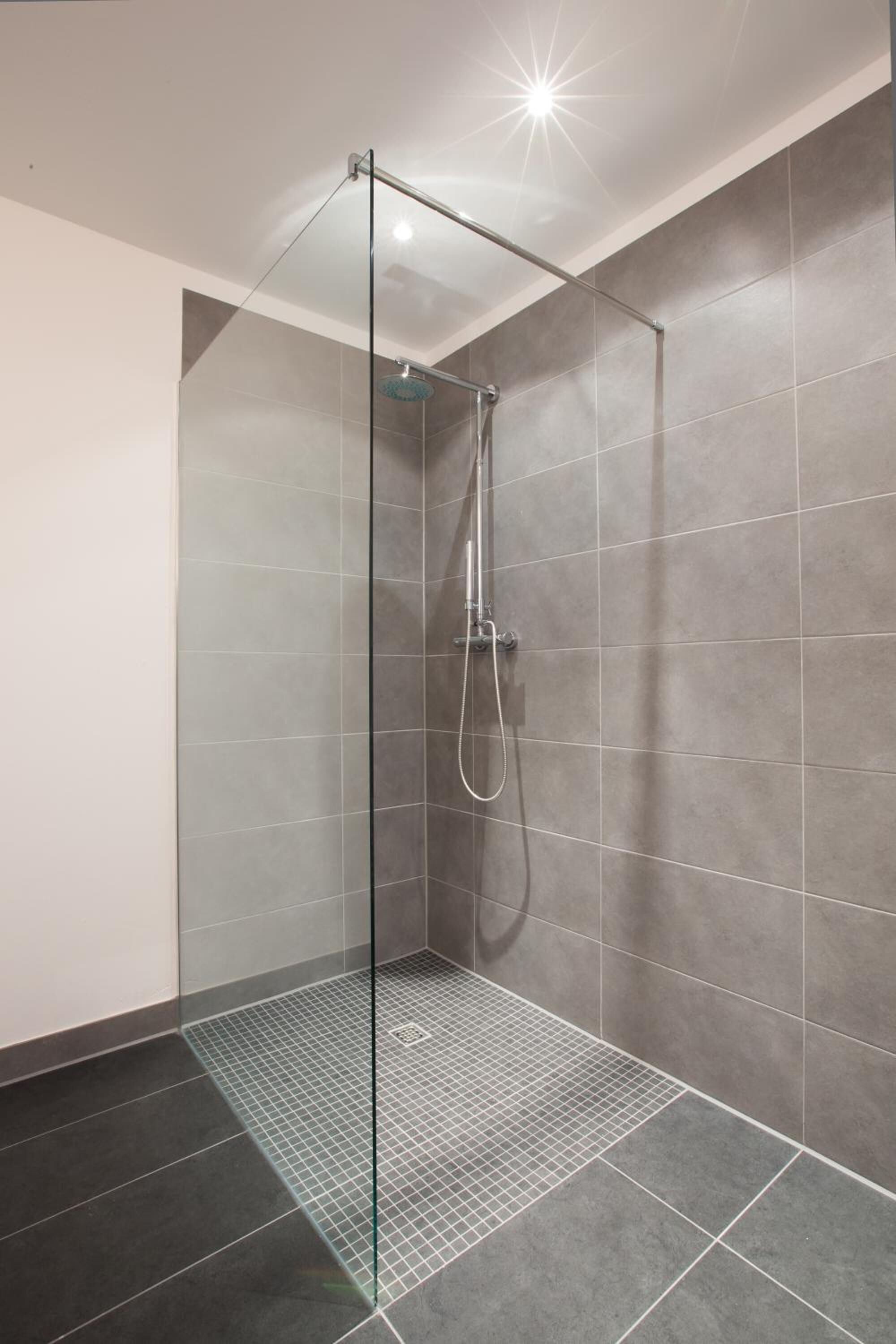 Une douche moderne dotée d’une porte en verre, de carreaux gris et d’un cadre en métal.