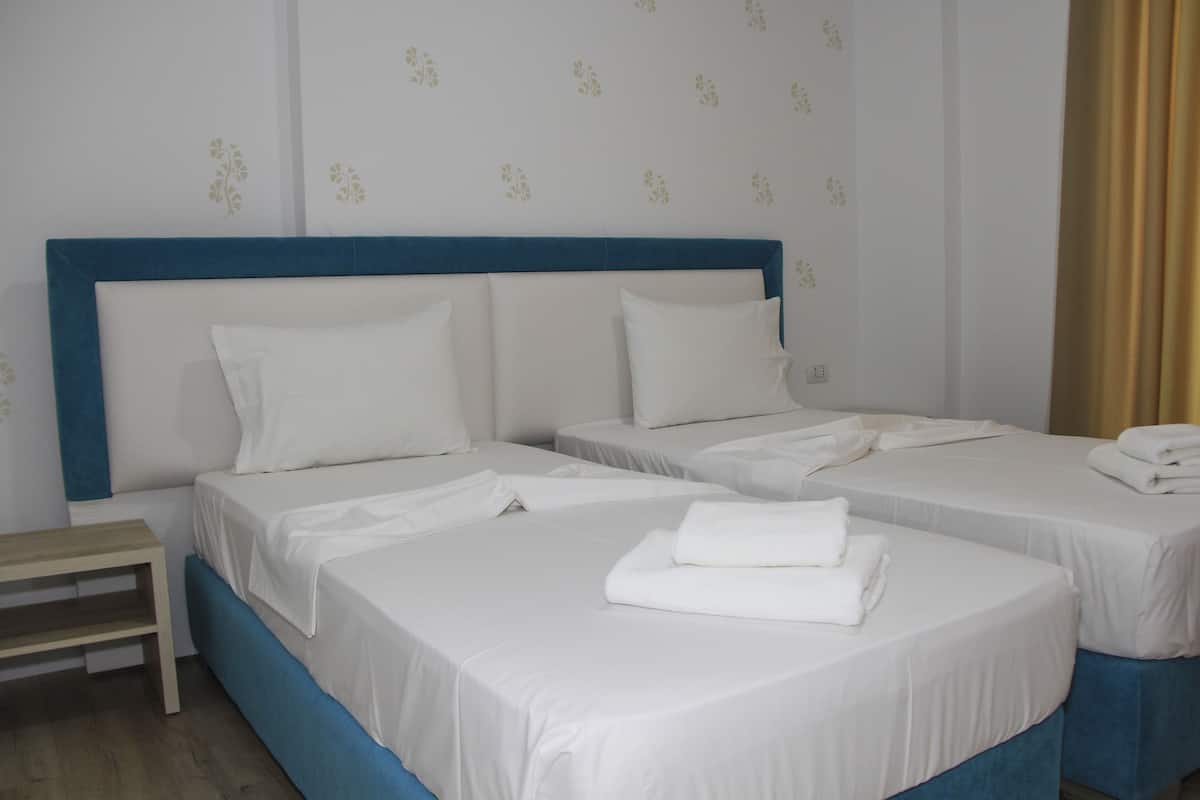 Une chambre d’hôtel avec deux lits, chacun doté de draps et d’oreillers blancs, d’une table de chevet en bois et d’une tête de lit bleue.