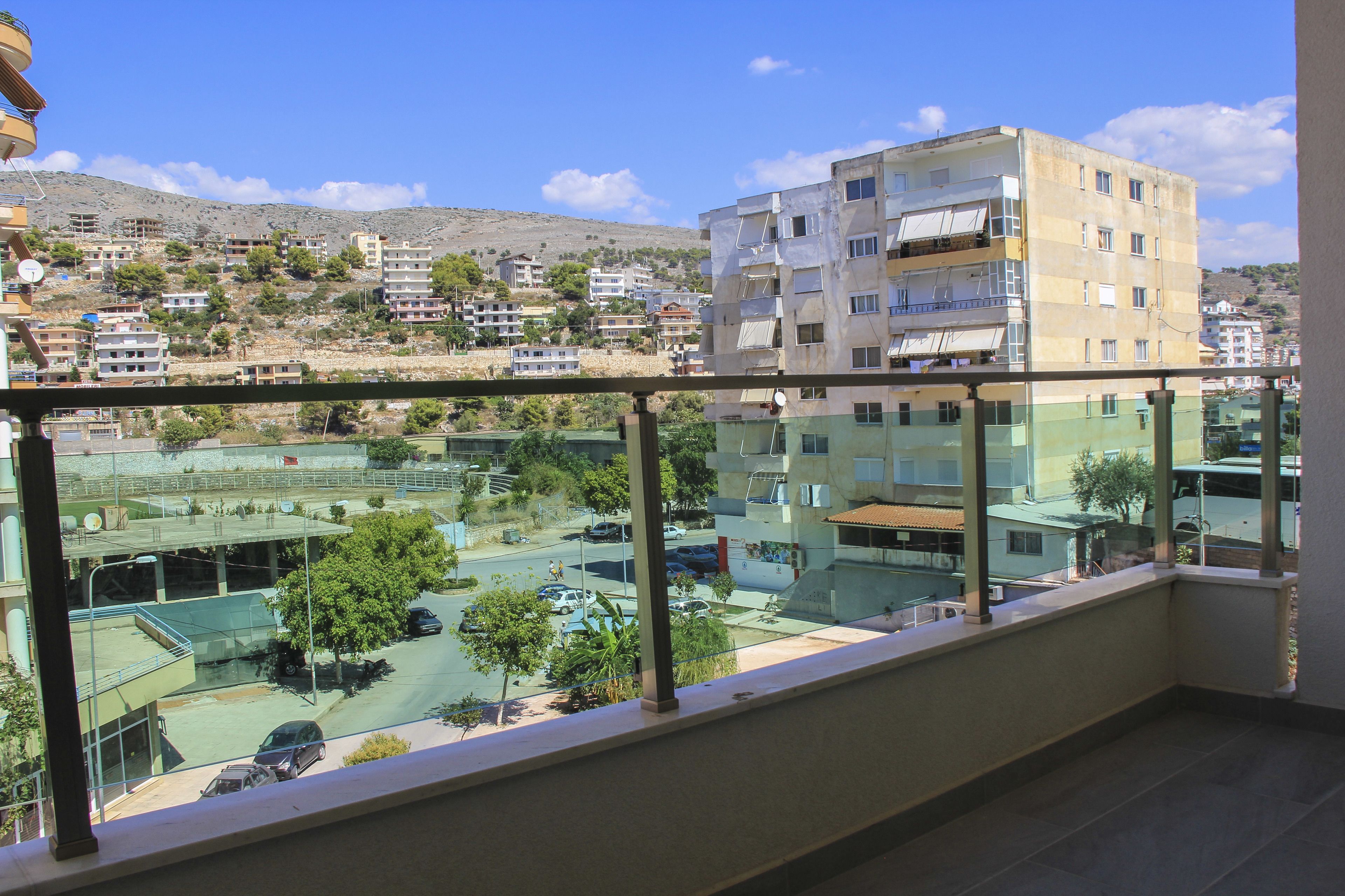 A balcony with a view of a residential area, including buildings and a road with parked cars.