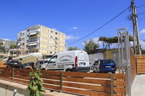 A white van parked near a wooden fence with a building in the background. - Maxi's Apartments (Sarandë)