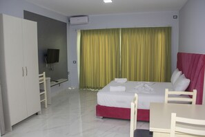 A hotel room with a bed, a desk, a chair, a wardrobe, and a television. - Maxi's Apartments (Sarandë)