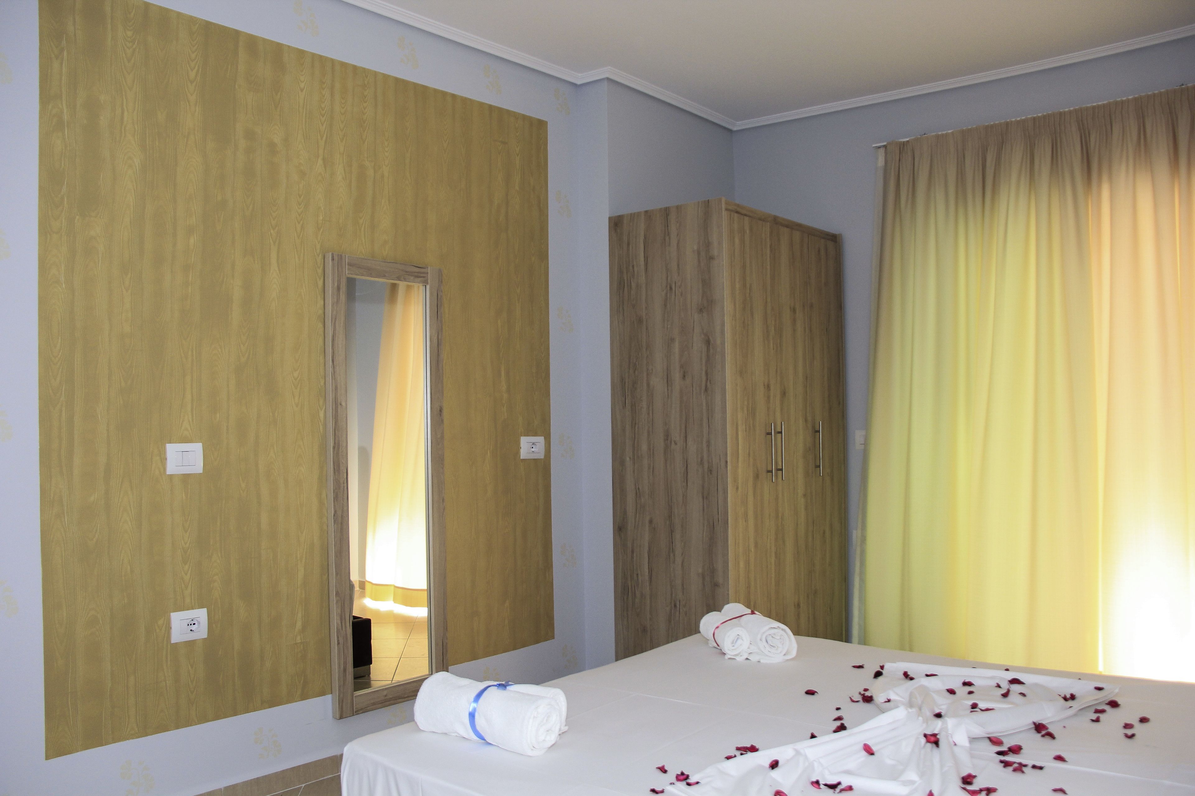 A hotel room with a large mirror, wooden wardrobe, and a bed with white linens and rose petals.