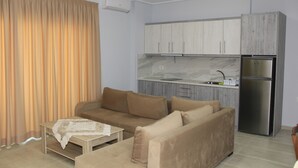 Una sala de estar moderna con un sofá beige, una mesita y una cocina con refrigerador y armarios.