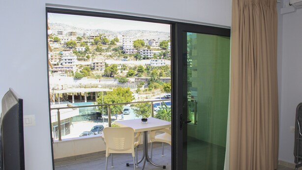 Un balcón con mesa y sillas, vistas a un barrio residencial y una puerta corrediza con cortina.