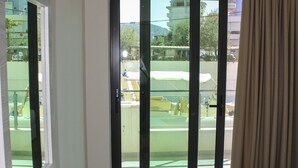 Habitación de hotel con cama, una silla, una mesa y puerta corrediza de vidrio que da a un balcón.