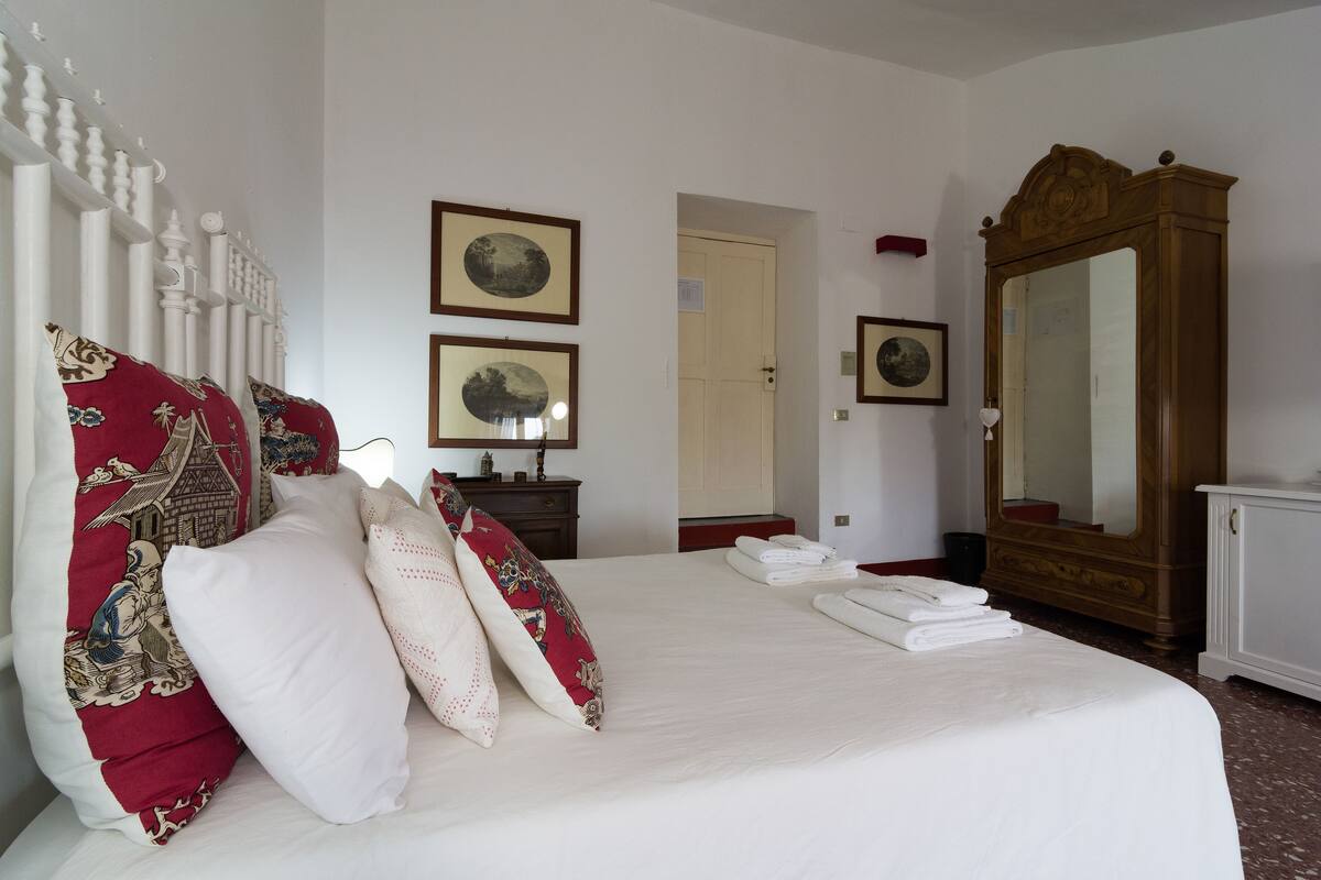 A neatly made bed with decorative pillows, a wooden wardrobe, and two framed pictures on the wall.