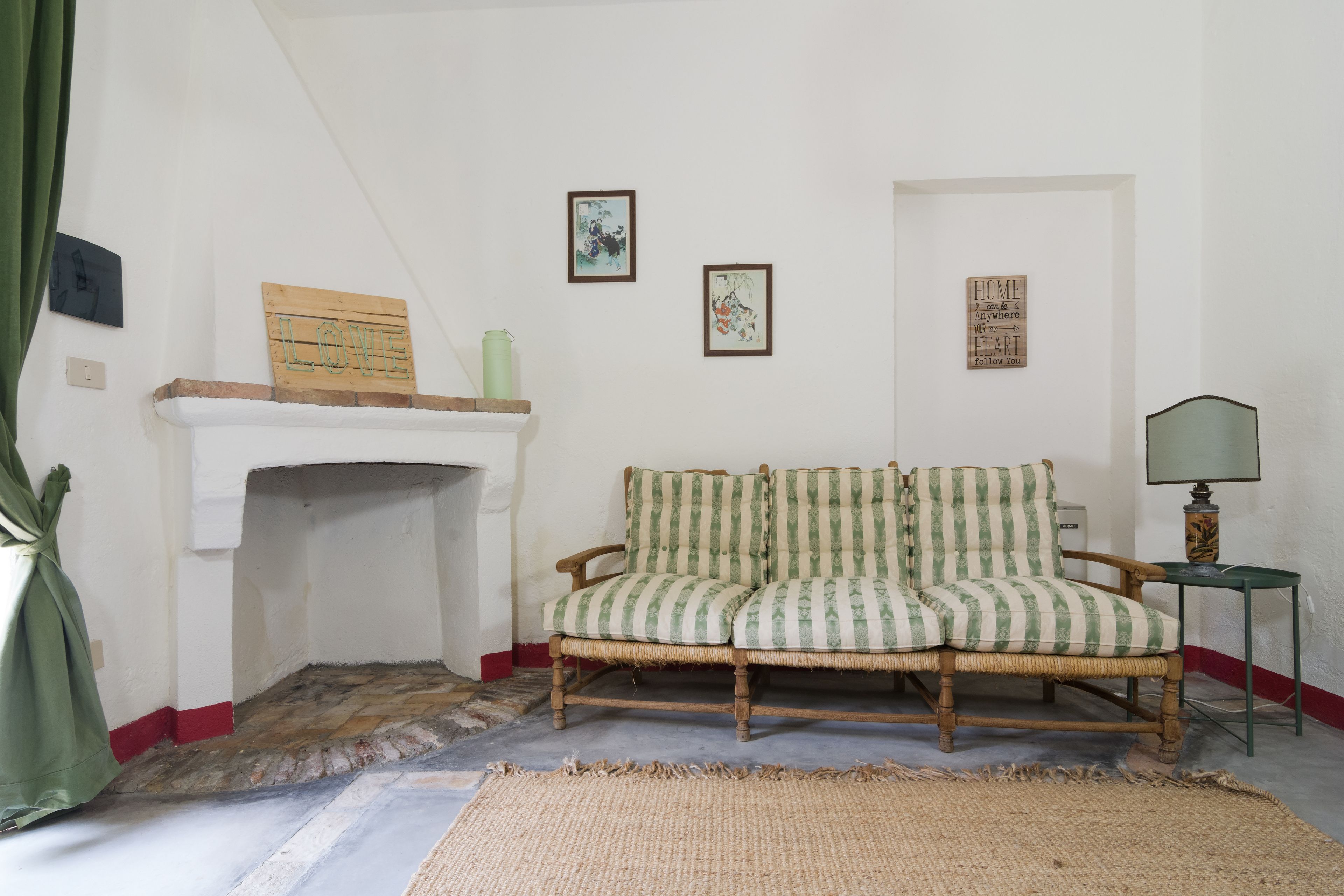 A room with a fireplace, a green-striped sofa, a small table with a lamp, and framed artwork on the walls.