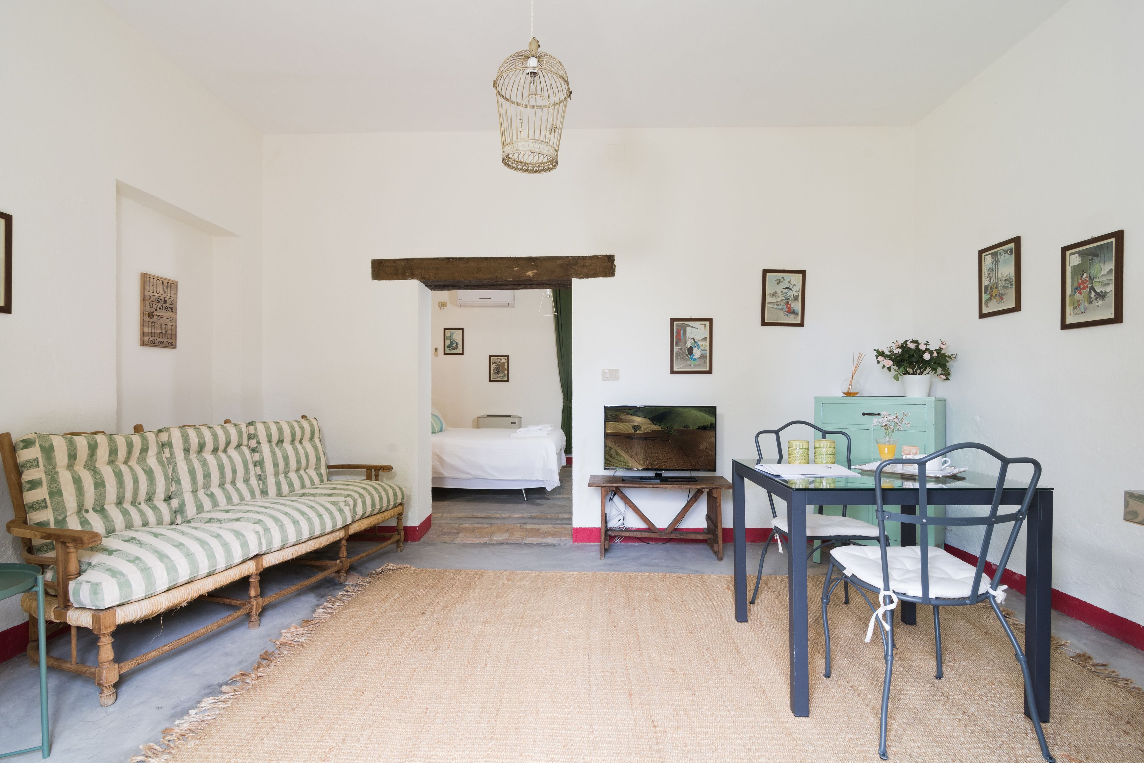 Una habitación con sofá, una mesa de comedor con sillas, televisor y cama al fondo.