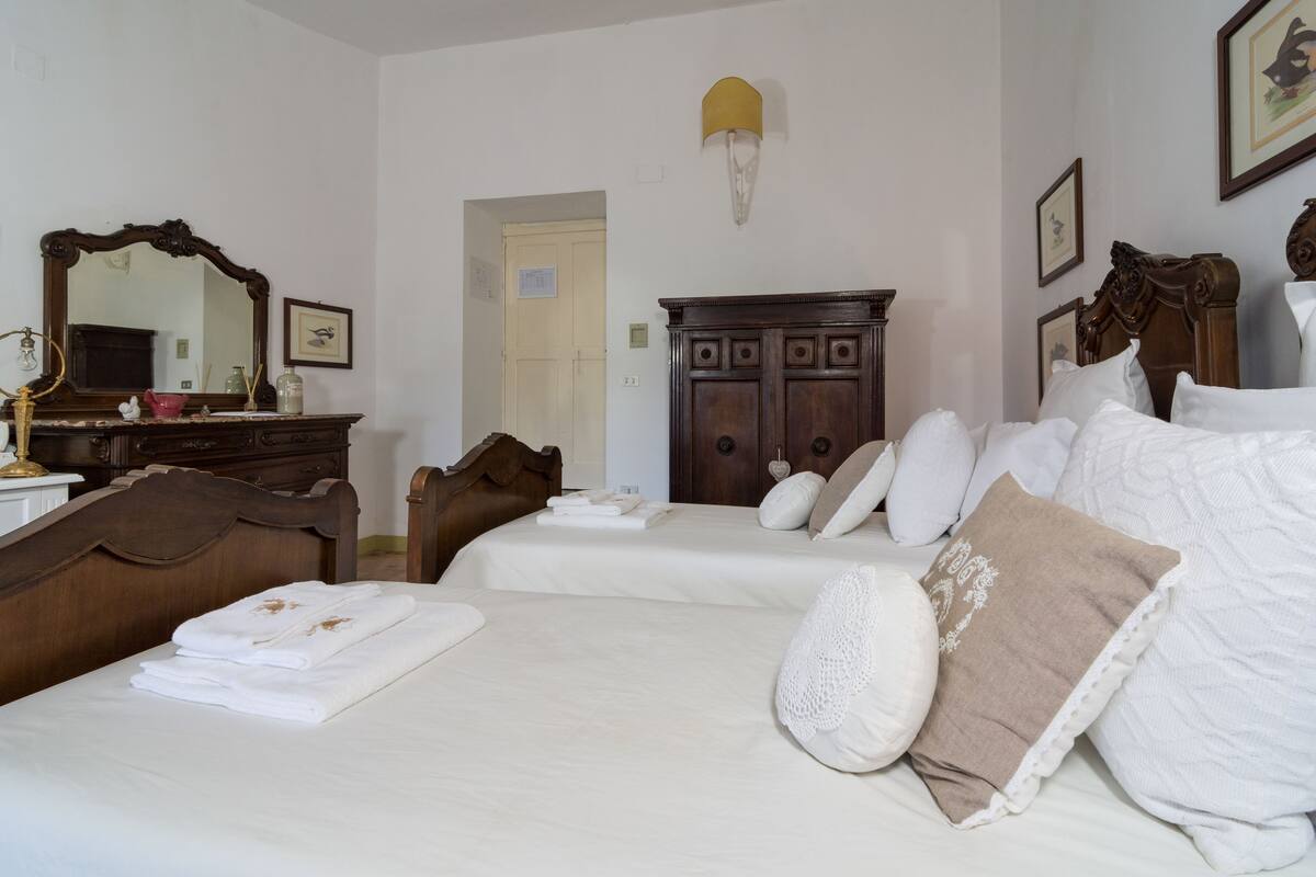 A hotel room with a large bed, a wooden dresser, a mirror, and a door leading to another room.