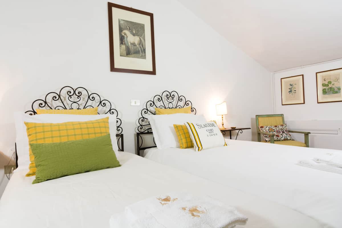 A hotel room with two beds, a framed picture on the wall, and a chair with a cushion.