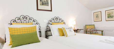 A hotel room with two beds, a framed picture on the wall, and a chair with a cushion.