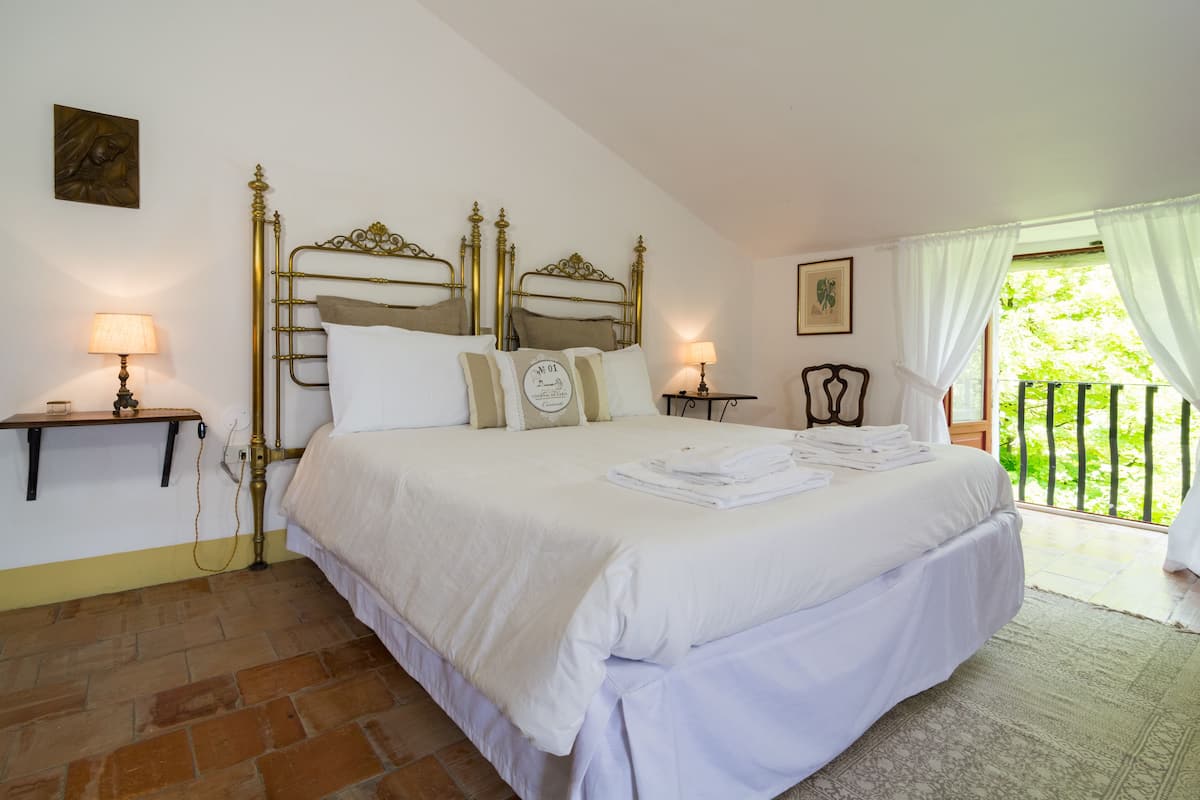 A neatly made bed with white linens, a brass headboard, and a small bedside table with a lamp.
