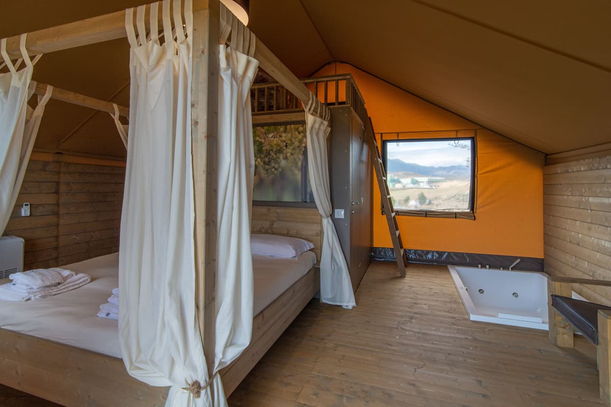 A room with a wooden bed, a window with a view, a bathtub, and a ladder.