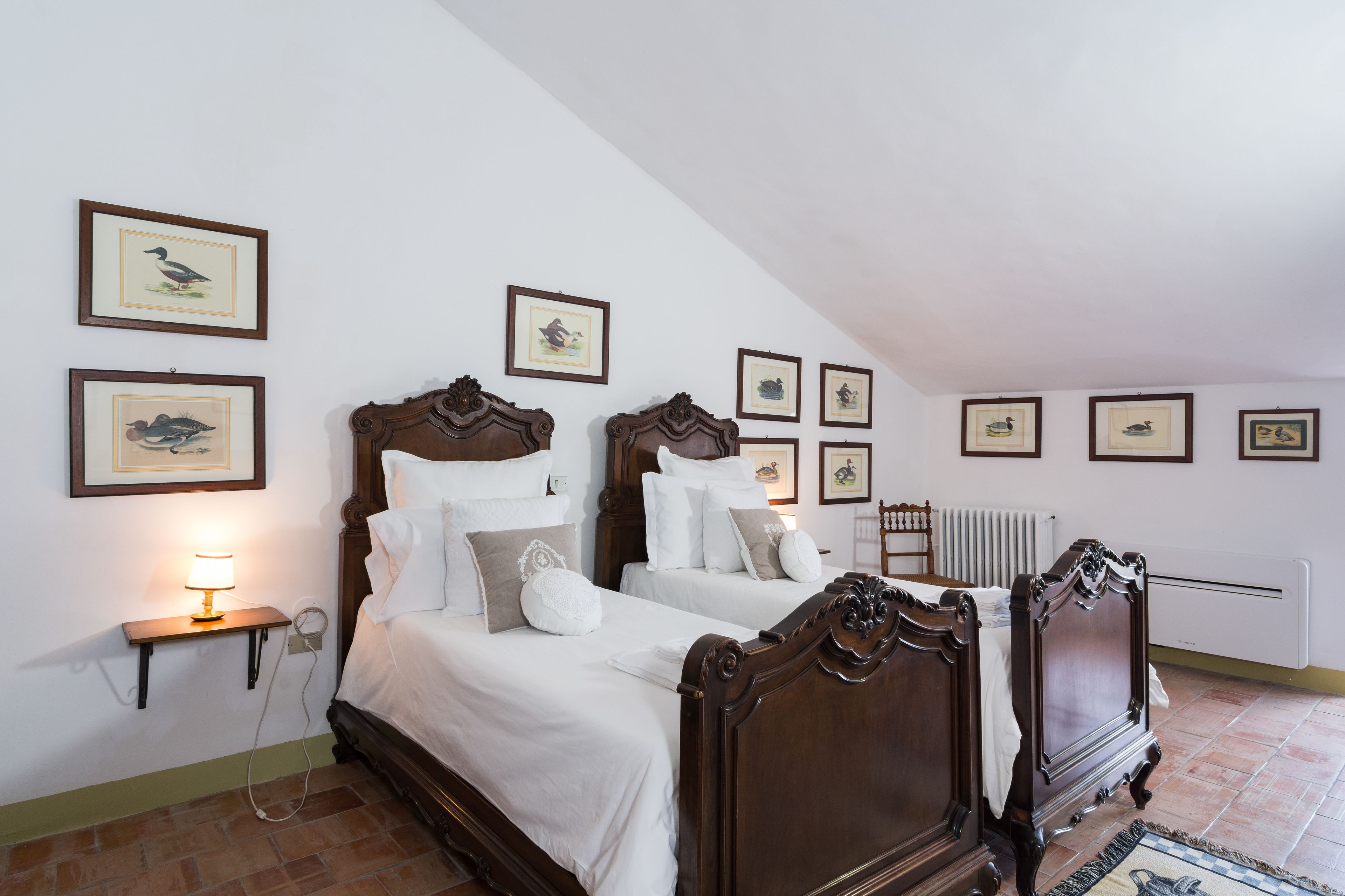Une chambre avec deux lits en bois, une literie blanche et plusieurs tableaux encadrés accrochés aux murs.