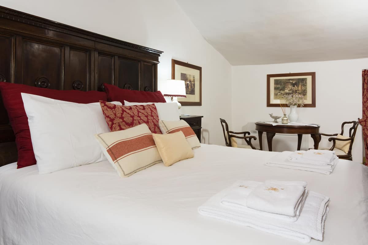 A neatly made bed with white and red bedding, a wooden headboard, and a small table with a vase and picture frame in the background.