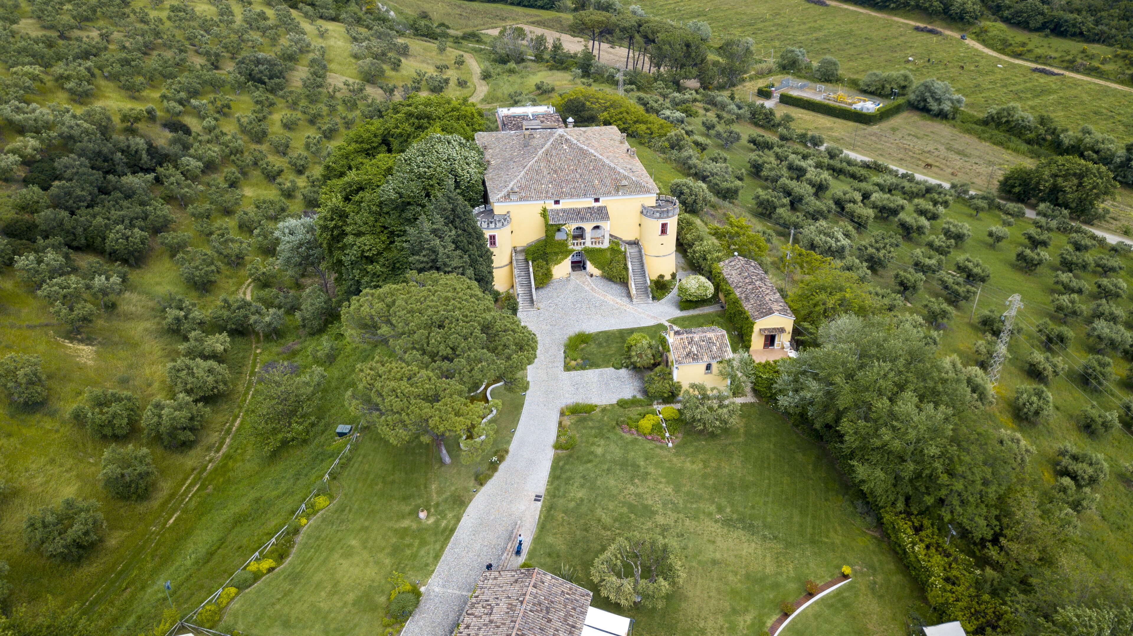 Luftaufnahme einer gelben Villa mit Innenhof, umgeben von üppigem Grün und einem gewundenen Weg.