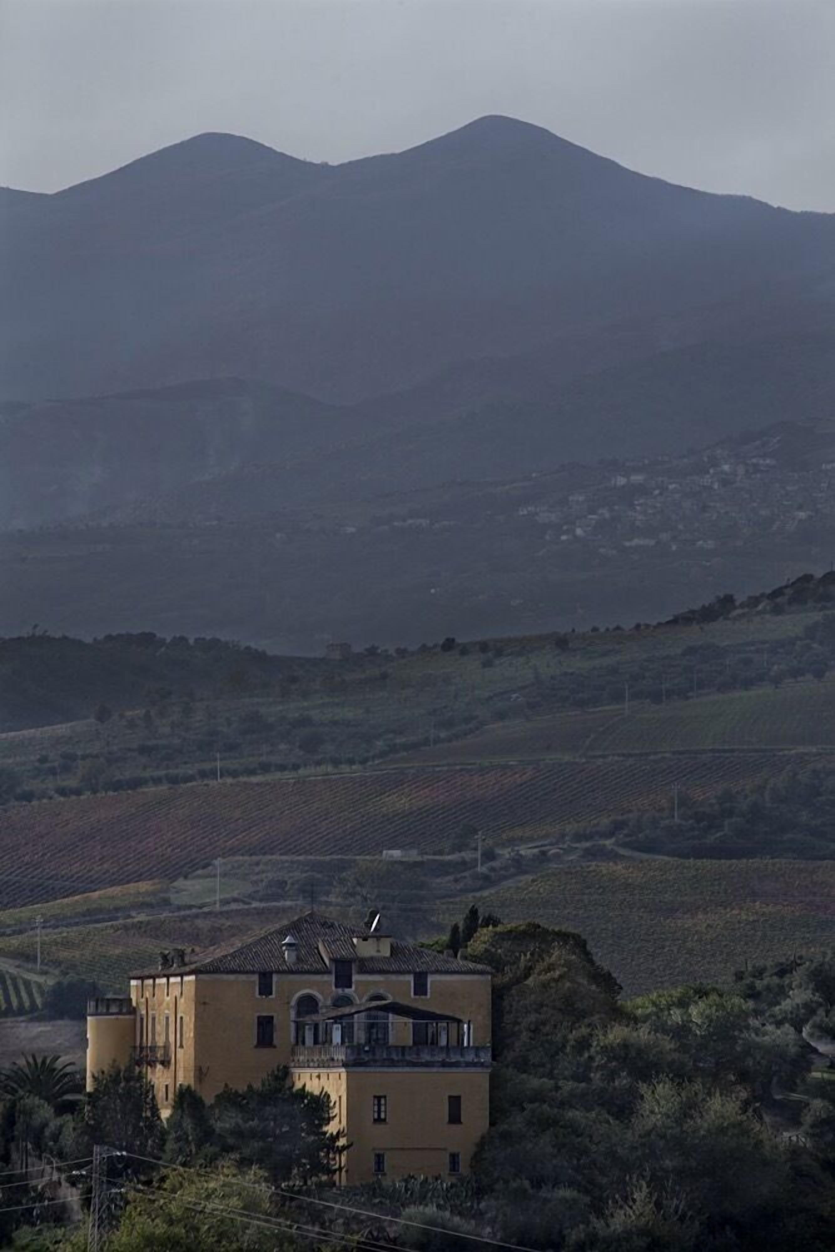 A building with a flat roof and a balcony, surrounded by a hilly landscape.