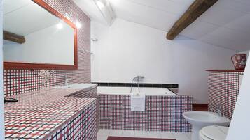A bathroom with a red and white checkered tile pattern, a large mirror, a bathtub, and a toilet.