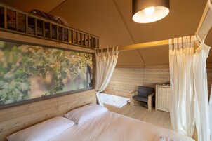 Un dormitorio con cama, ventana con vistas a follaje, cabecero de madera, mesita de noche y un banco.
