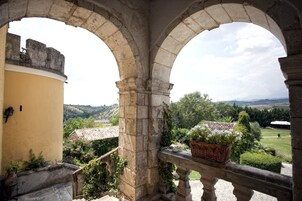 Un balcón de piedra con arcos que da a un jardín y un paisaje lejano.