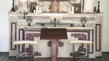 Una capilla con columnas ornamentadas, un cuadro religioso, velas y dos bancos.