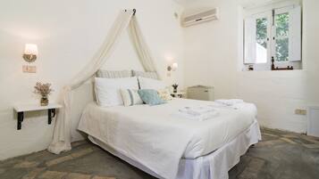 A bedroom with a canopy bed, a bedside table with a lamp, a shelf with a vase, and a window with a view of trees.