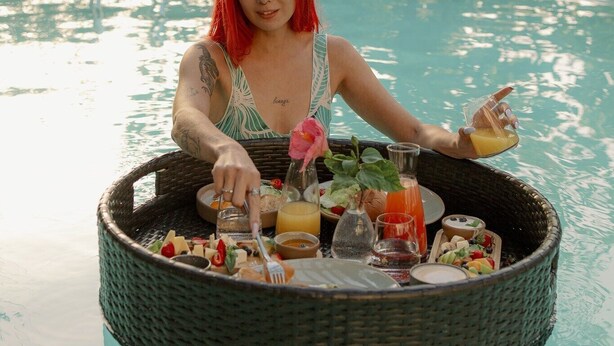 A person sitting by a pool with a floating tray of food and drinks. - Zebra  (Tivat)